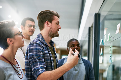 Buy stock photo Shot of a group of designers brainstorming with notes on a glass wall in an office