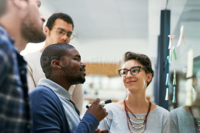 Buy stock photo Shot of a group of designers brainstorming with notes on a glass wall in an office
