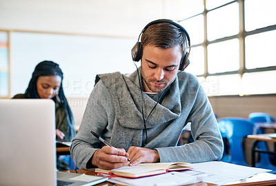 Buy stock photo Cropped shot of a handsome young university student taking notes while sitting in class