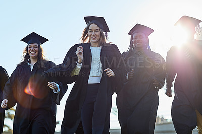 Buy stock photo Shot of a group of students running together in a row on graduation day