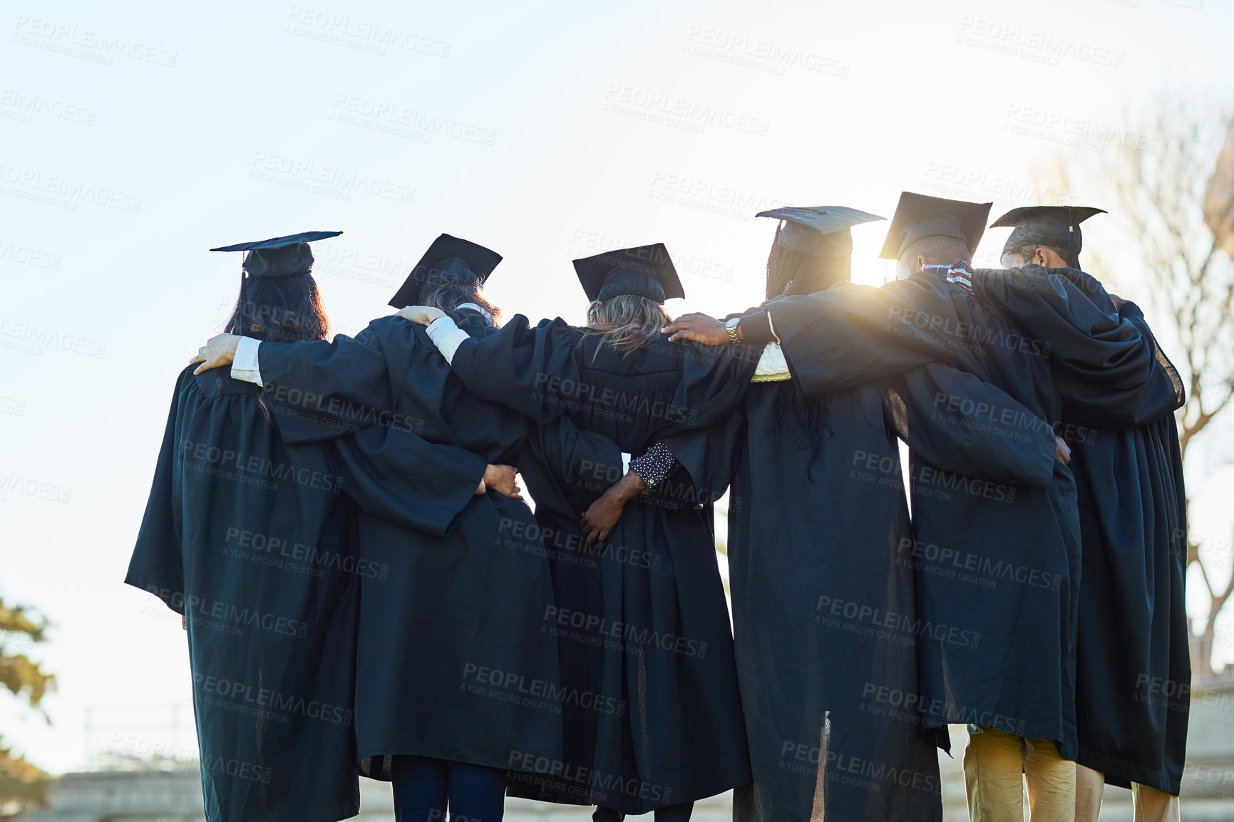 Buy stock photo Rearview shot of a group of students standing in a row on graduation day