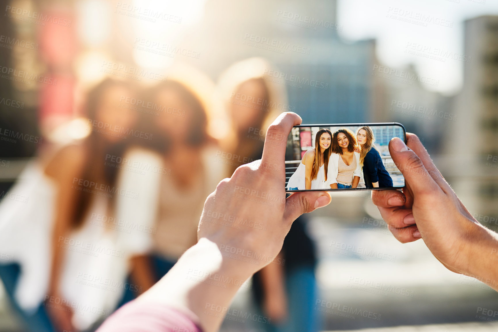 Buy stock photo Shot of an unrecognizable man taking a picture with a smartphone of female friends outside