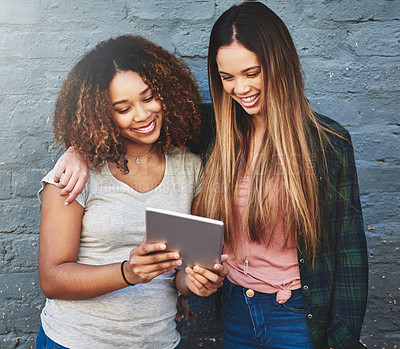 Buy stock photo Shot of two young women standing outdoors and using a digital tablet against a gray wall