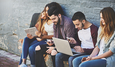 Buy stock photo Shot of a group of young friends using their wireless devices together outdoors