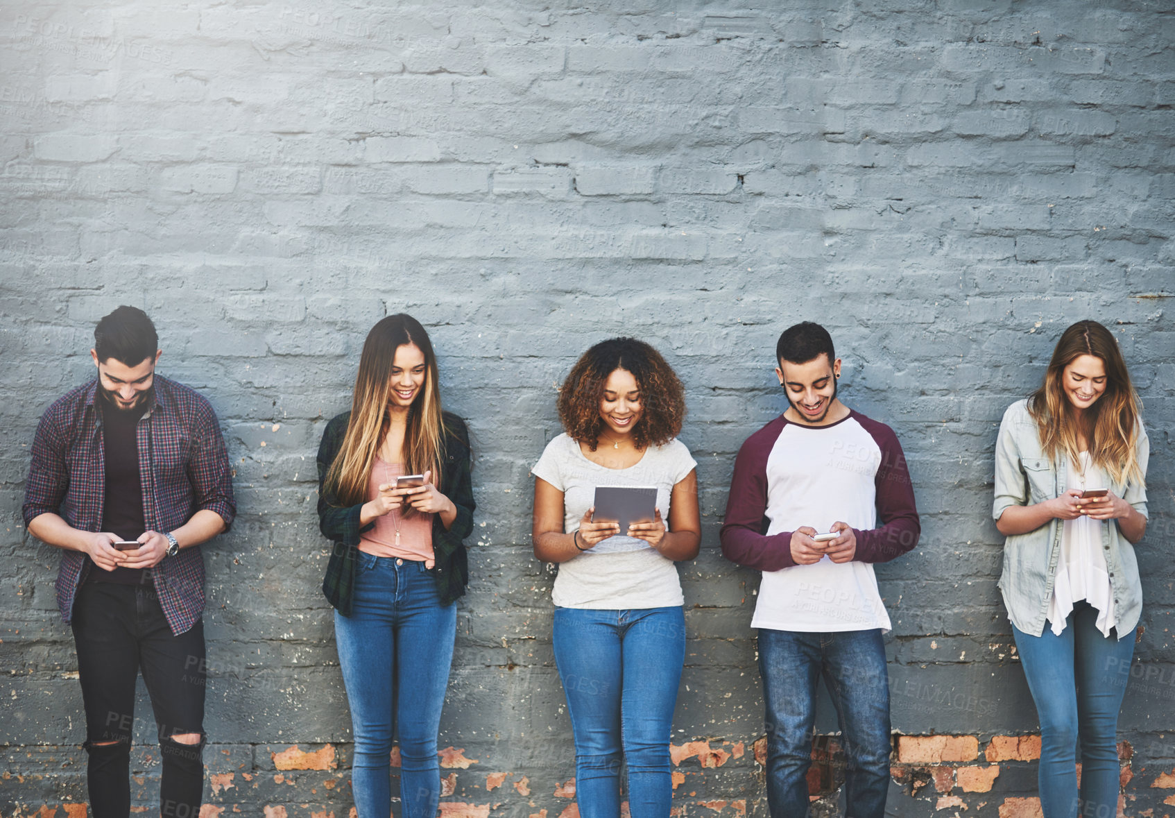 Buy stock photo Shot of a group of young people using their wireless devices together outdoors