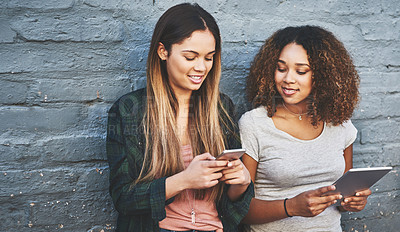 Buy stock photo Shot of two young women standing outdoors and using their digital tablets against a gray wall