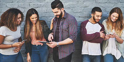 Buy stock photo Shot of a group of young friends using their wireless devices together outdoors