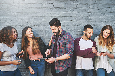 Buy stock photo Shot of a group of young friends using their wireless devices together outdoors