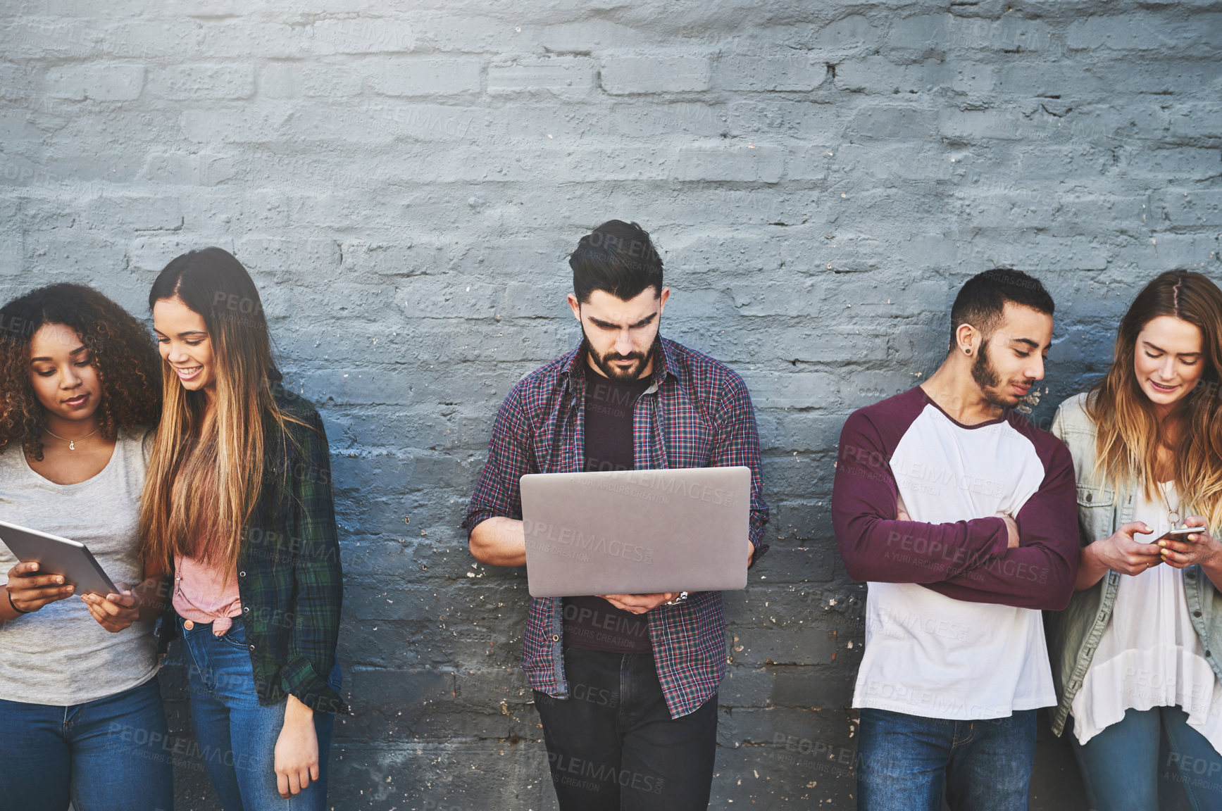 Buy stock photo Shot of a group of young friends using their wireless devices together outdoors