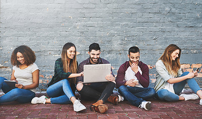 Buy stock photo Shot of a group of young friends using their wireless devices together outdoors