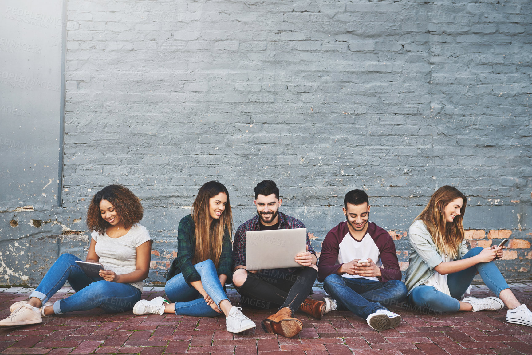 Buy stock photo Shot of a group of young friends using their wireless devices together outdoors