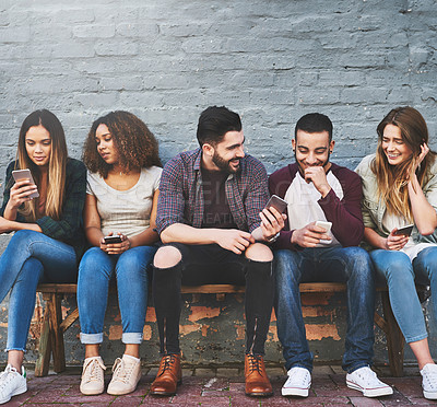 Buy stock photo Shot of a group of young friends using their mobile phones outdoors