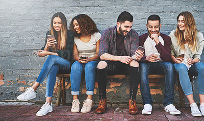 Buy stock photo Shot of a group of young friends using their mobile phones outdoors