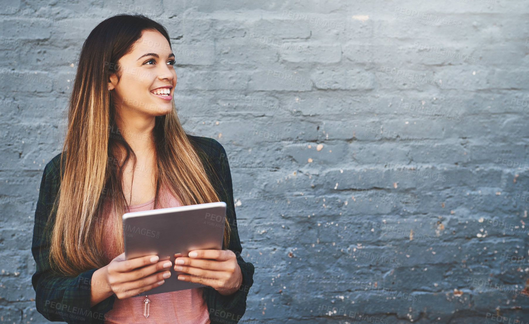 Buy stock photo Shot of a young woman standing outdoors and using a digital tablet against a gray wall