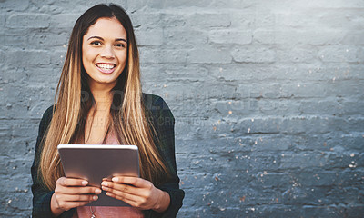 Buy stock photo Portrait of a young woman standing outdoors and using a digital tablet against a gray wall