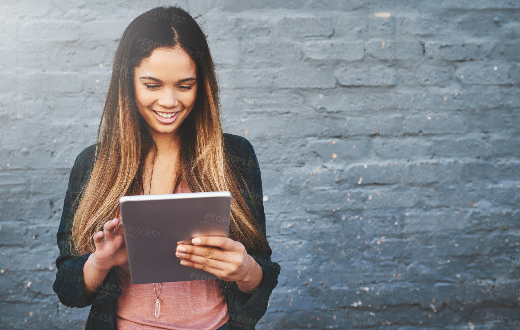 Buy stock photo Shot of a young woman standing outdoors and using a digital tablet against a gray wall