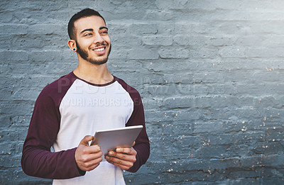 Buy stock photo Shot of a young man standing outdoors and using a digital tablet against a gray wall