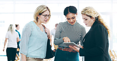 Buy stock photo Cropped shot of three corporate businesswomen standing in a huddle with digital tablets in hand