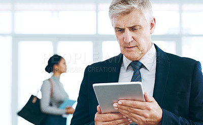 Buy stock photo Cropped shot of a handsome mature businessman using a tablet in the office with his colleagues in the background