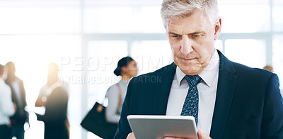 Buy stock photo Cropped shot of a handsome mature businessman using a tablet in the office with his colleagues in the background
