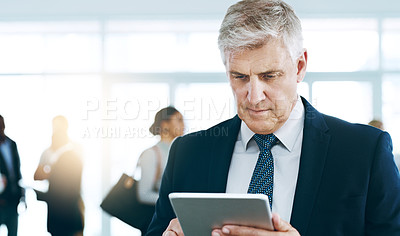 Buy stock photo Cropped shot of a handsome mature businessman using a tablet in the office with his colleagues in the background