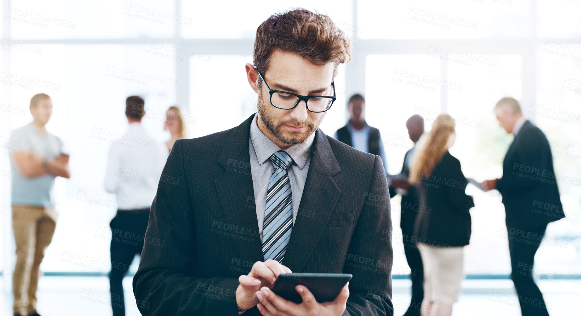 Buy stock photo Cropped shot of a handsome businessman using a tablet in the office with his colleagues in the background