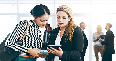 Buy stock photo Cropped shot of two corporate businesswomen standing in a huddle with digital tablets in hand
