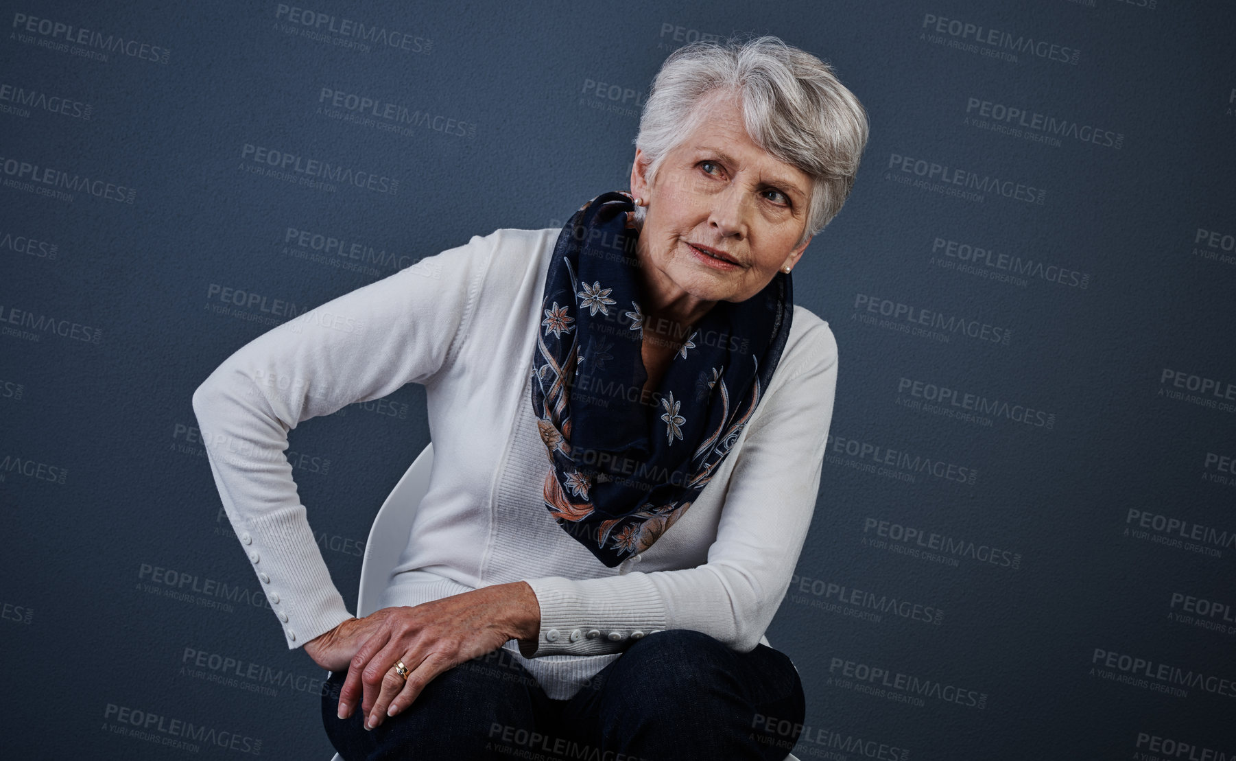 Buy stock photo Studio shot of a elderly woman sitting down with her one hand on her hip while looking onto the distance