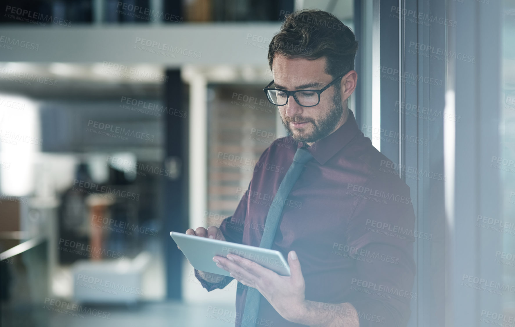 Buy stock photo Shot of a young businessman using a digital tablet in a modern office