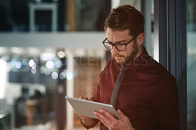 Buy stock photo Shot of a young businessman using a digital tablet in a modern office