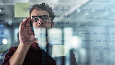 Buy stock photo Shot of a young businessman brainstorming with sticky notes on a glass wall in a modern office