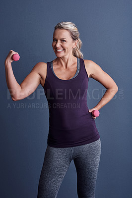 Buy stock photo Studio portrait of an attractive mature woman working out with dumbbells against a blue background