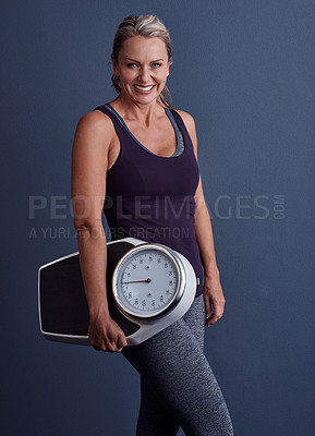 Buy stock photo Studio portrait of an attractive mature woman holding a weightscale against a blue background