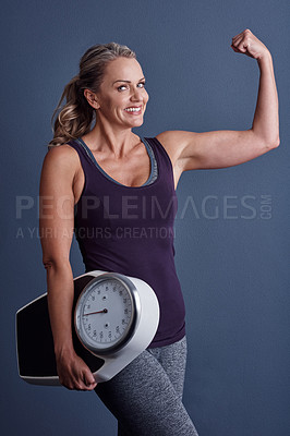Buy stock photo Studio portrait of an attractive mature woman holding a weightscale and flexing against a blue background
