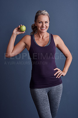 Buy stock photo Studio portrait of an attractive mature woman holding an apple against a blue background