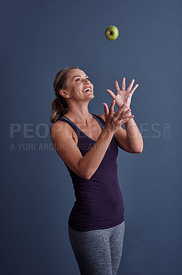 Buy stock photo Studio shot of an attractive mature woman throwing an apple against a blue background