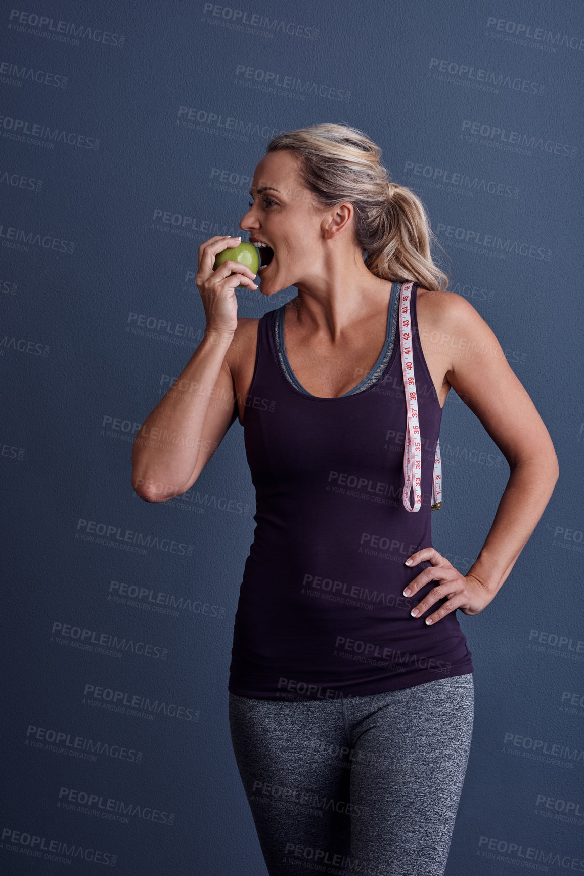 Buy stock photo Studio shot of an attractive mature woman biting into an apple against a blue background