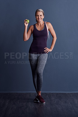 Buy stock photo Studio portrait of an attractive mature woman holding an apple against a blue background