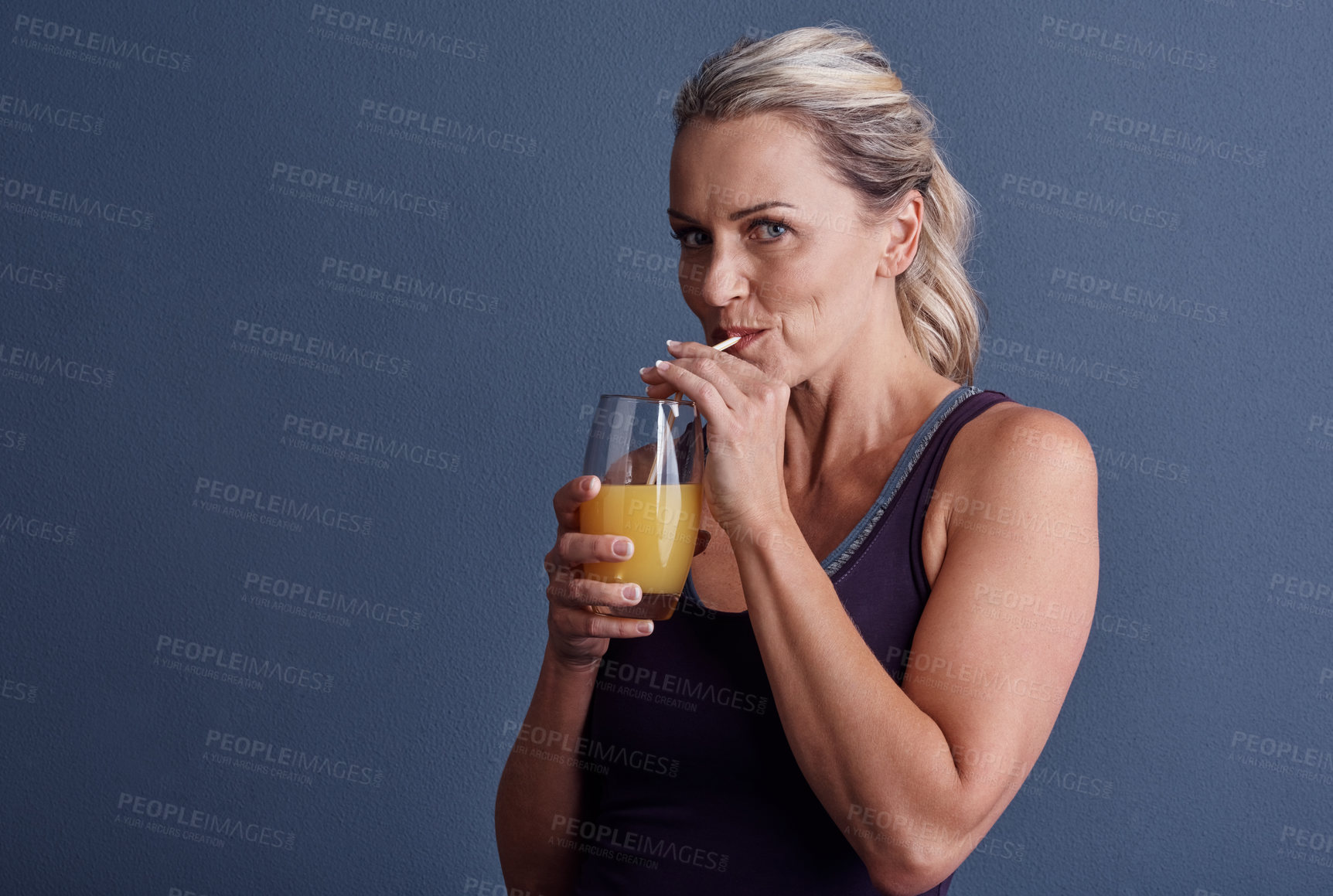 Buy stock photo Studio portrait of an attractive mature woman in sportswear drinking orange juice against a blue background