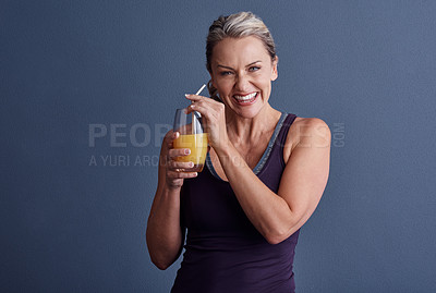 Buy stock photo Studio portrait of an attractive mature woman in sportswear drinking orange juice against a blue background