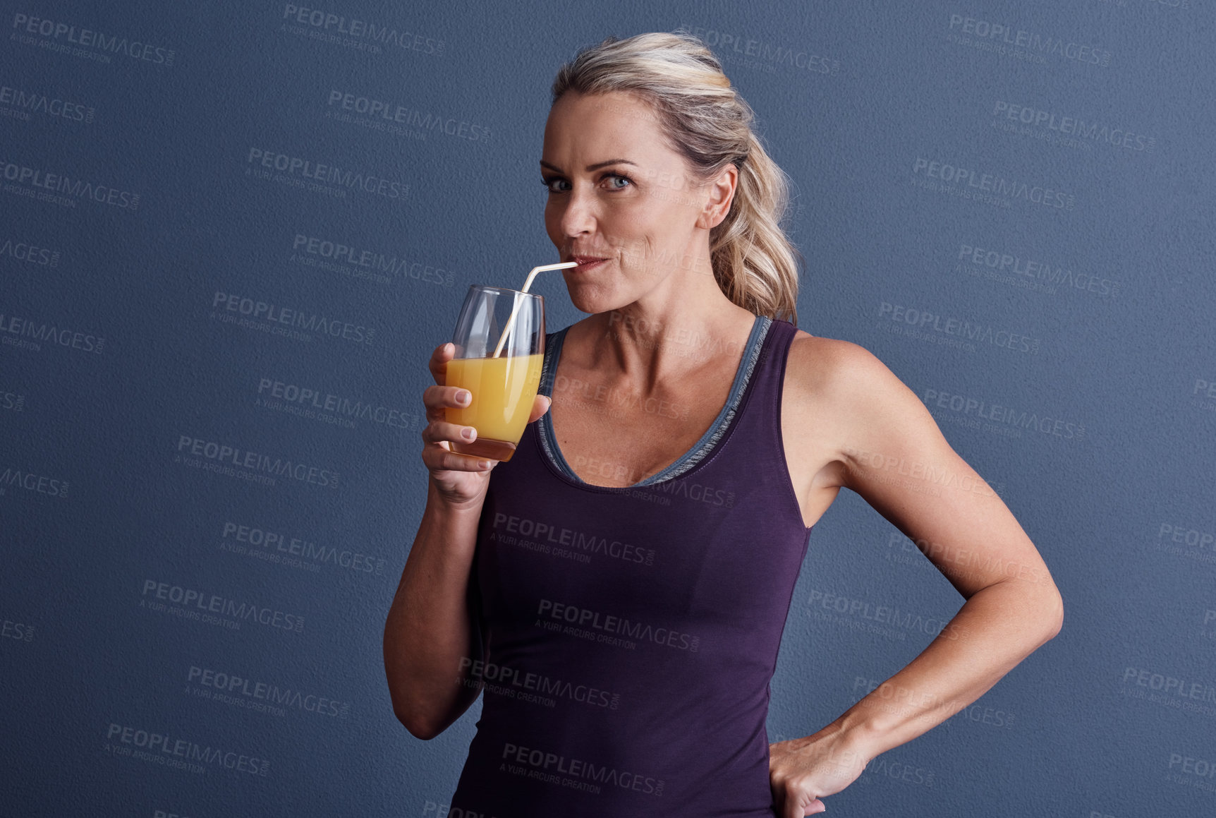 Buy stock photo Studio portrait of an attractive mature woman in sportswear drinking orange juice against a blue background