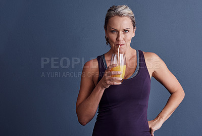 Buy stock photo Studio portrait of an attractive mature woman in sportswear drinking orange juice against a blue background