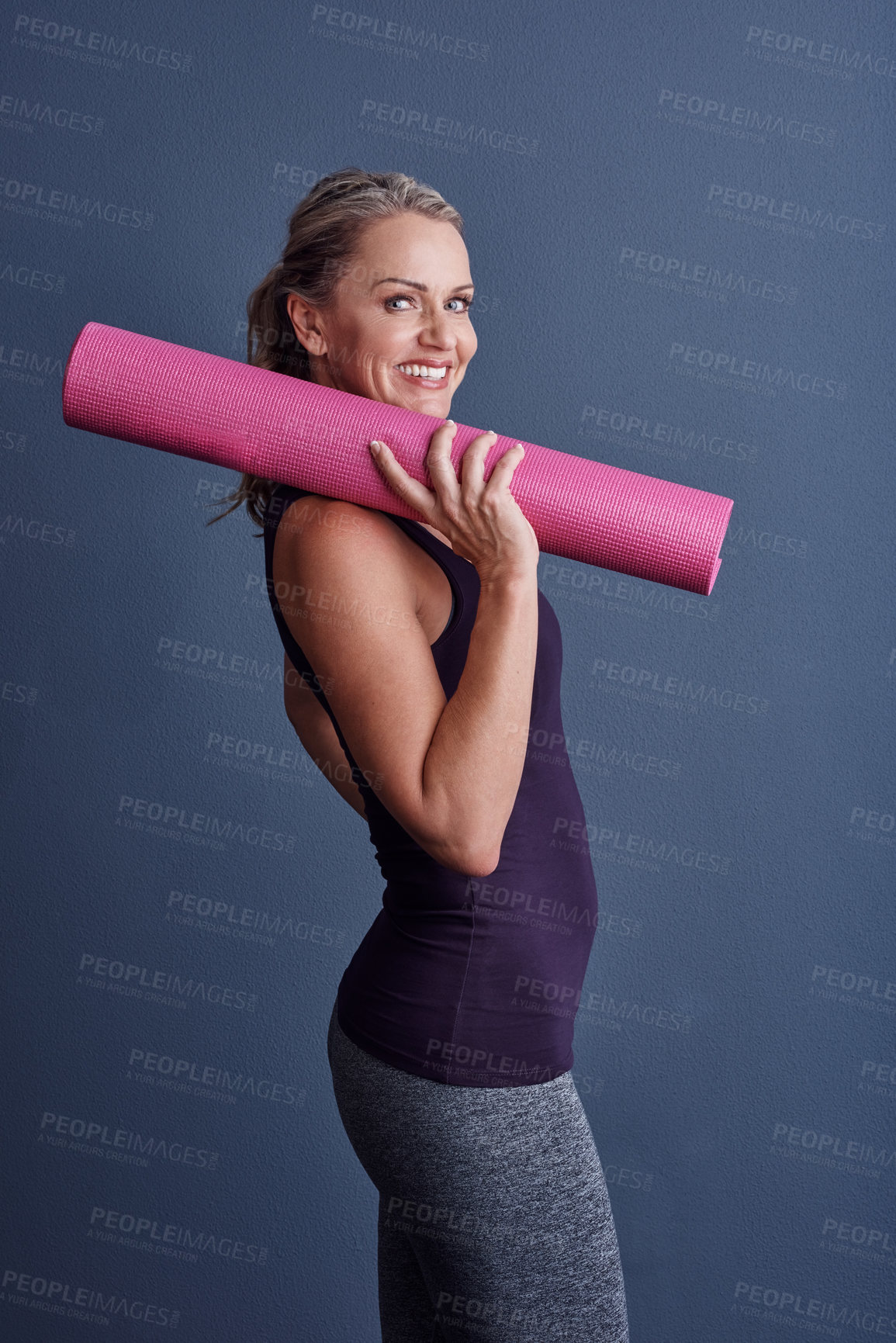 Buy stock photo Studio portrait of an attractive mature woman in sportswear holding an exercise mat against a blue background