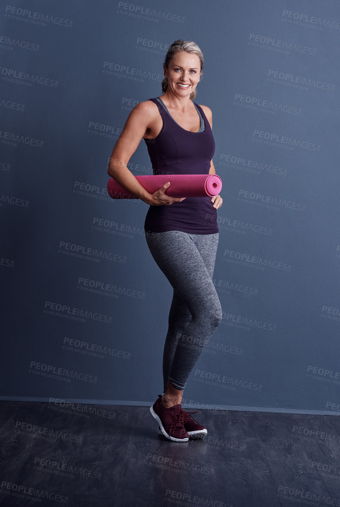 Buy stock photo Studio portrait of an attractive mature woman in sportswear holding an exercise mat against a blue background
