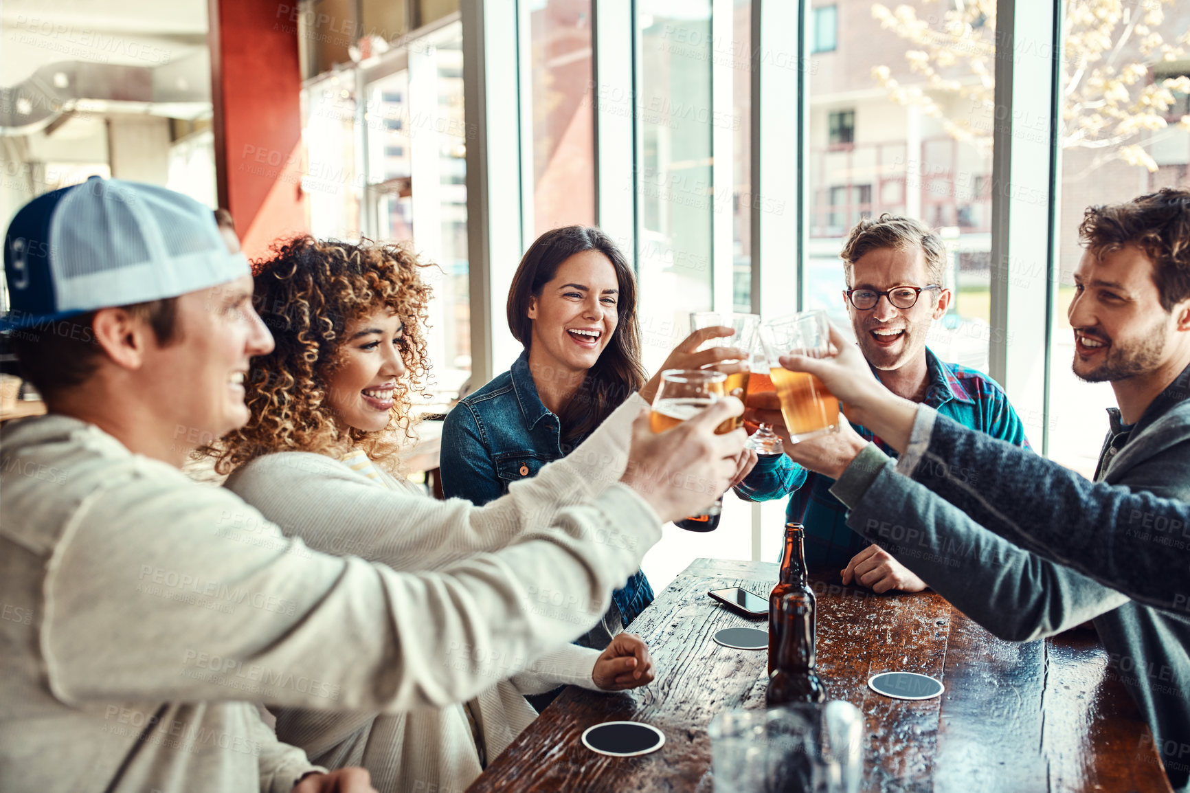 Buy stock photo Cheers, beer and friends at restaurant in celebration of birthday event in urban New York bar. Group of people with smile for happiness and gathering together with alcohol beverage at summer lunch