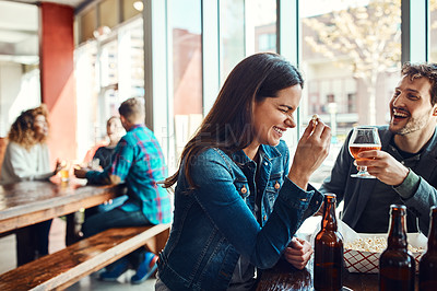 Buy stock photo Cropped shot of a young couple having drinks in a bar with people blurred in the background