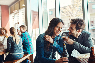 Buy stock photo Cropped shot of a young couple having drinks in a bar with people blurred in the background