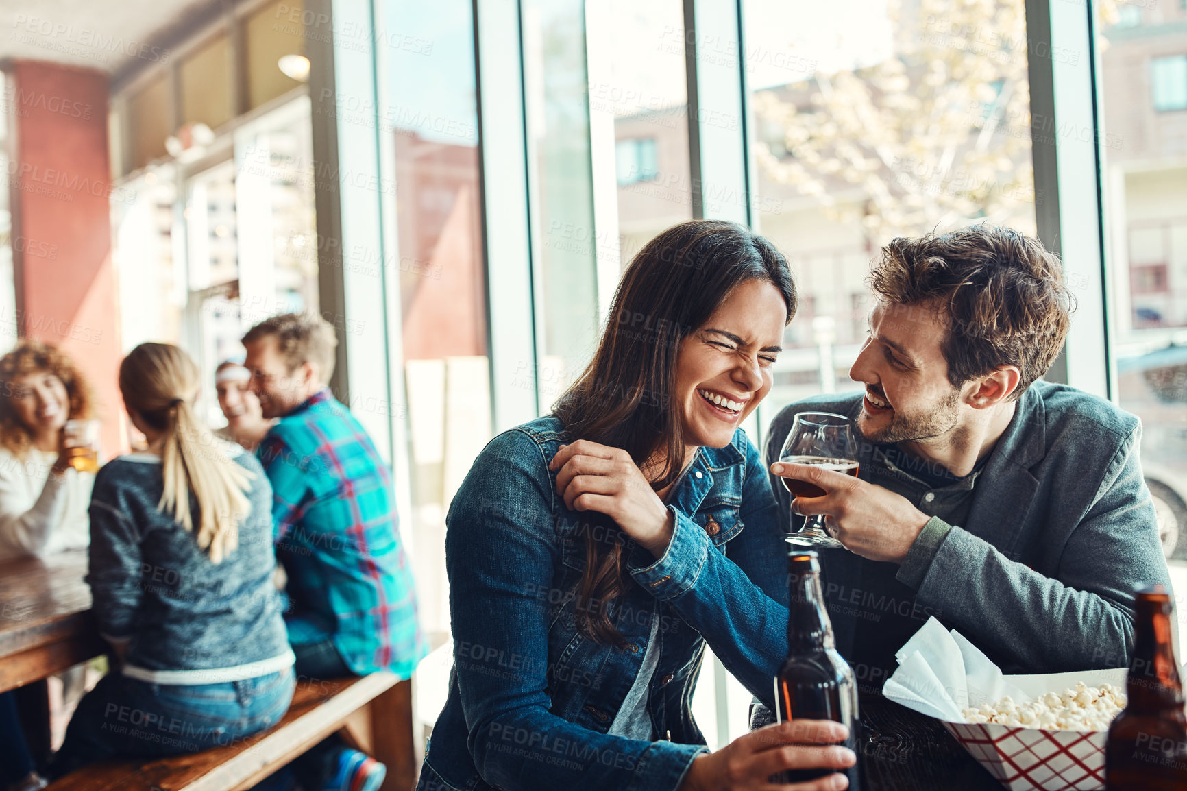 Buy stock photo Cropped shot of a young couple having drinks in a bar with people blurred in the background