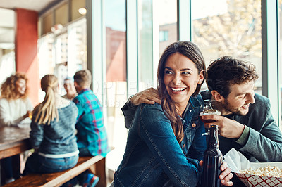 Buy stock photo Cropped shot of a young couple having drinks in a bar with people blurred in the background