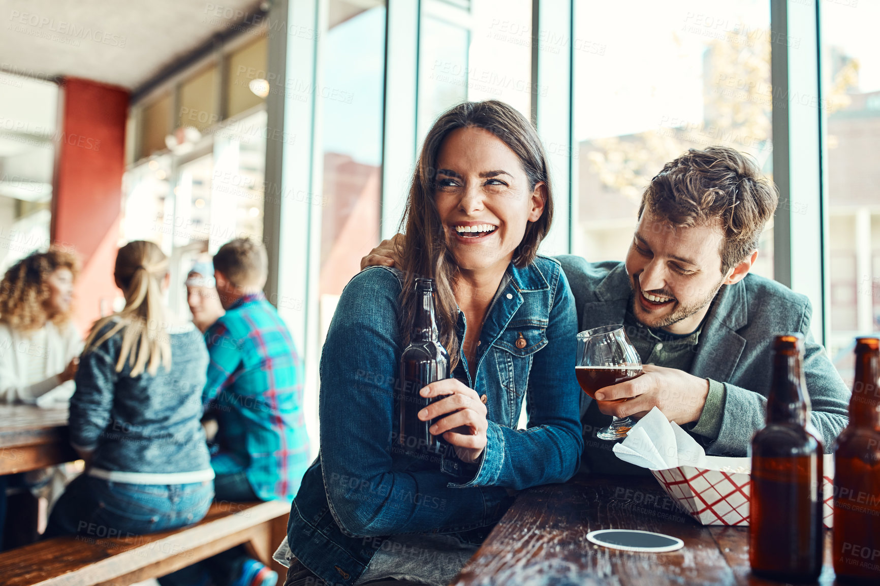 Buy stock photo Cropped shot of a young couple having drinks in a bar with people blurred in the background